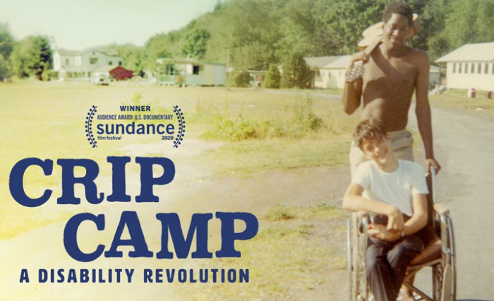 Movie poster for Crip Camp: A Disability Revolution. A young white boy in a wheelchair being pushed by a young black boy with an acoustic guitar in his hand